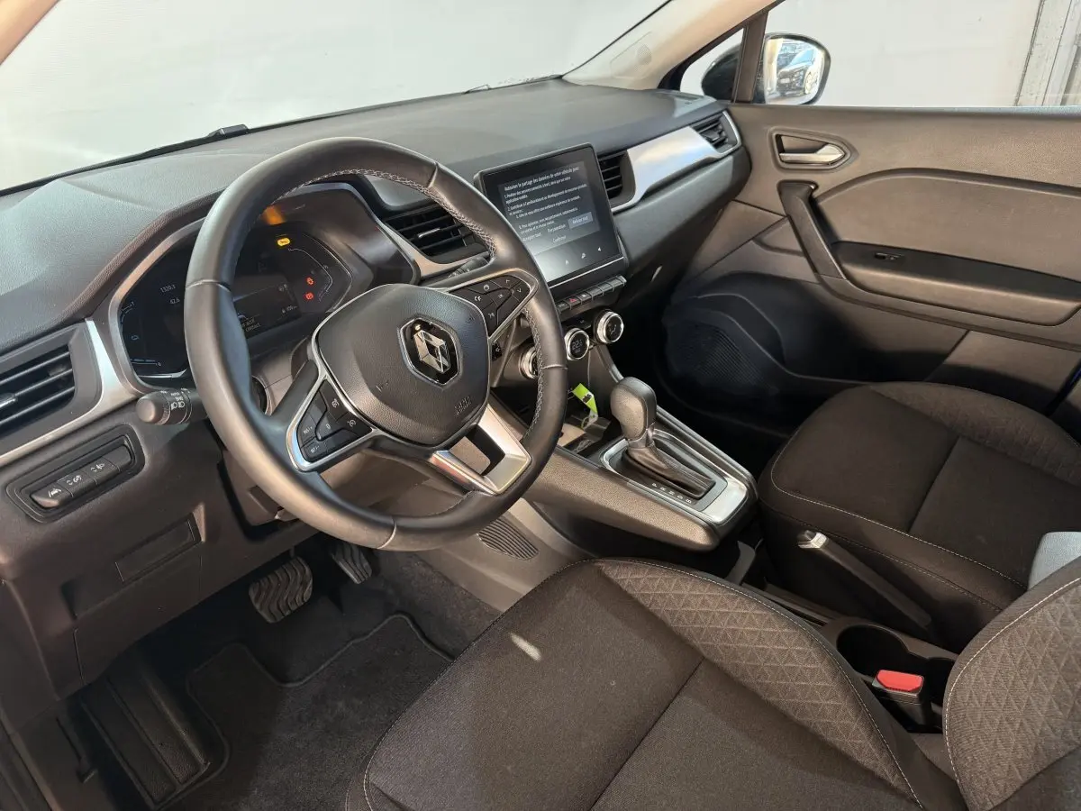 Vue intérieure côté conducteur du Renault Captur 2024, volant cuir multifonctions et écran tactile central visible.