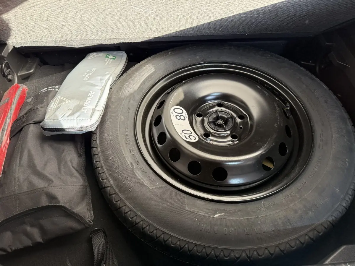 Gros plan sur la roue de secours noire dans le coffre du Renault Captur bleu 2024, avec trousse de secours à côté.