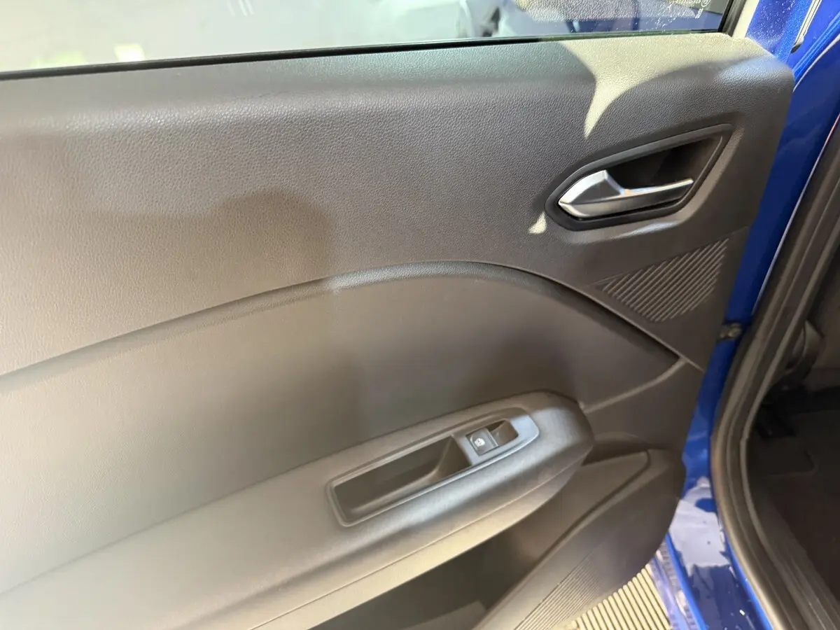 Détail de la porte avant gauche intérieure noire du Renault Captur bleu 2024, avec poignée argentée et commande de vitre.