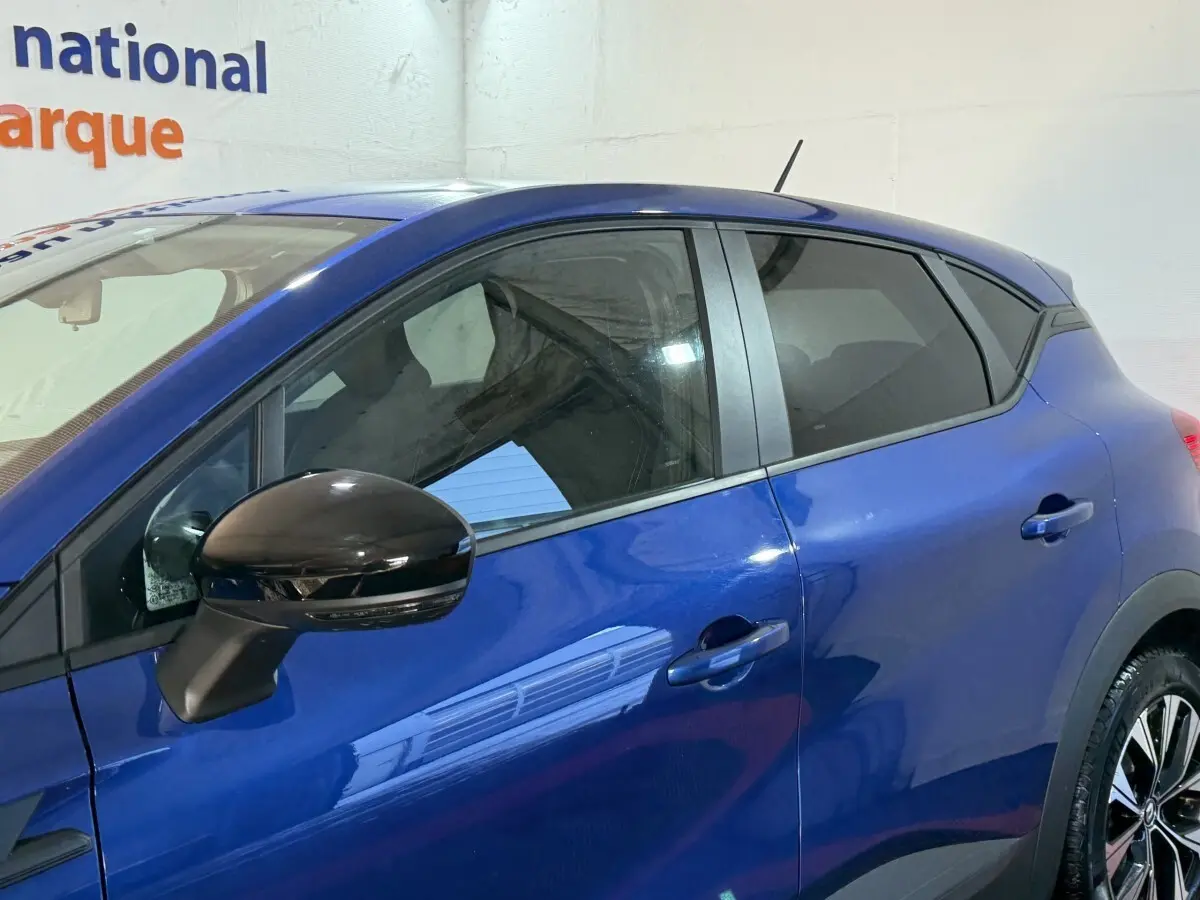 Vue latérale gauche du Renault Captur bleu 2024 avec rétroviseur noir brillant et vitres teintées.