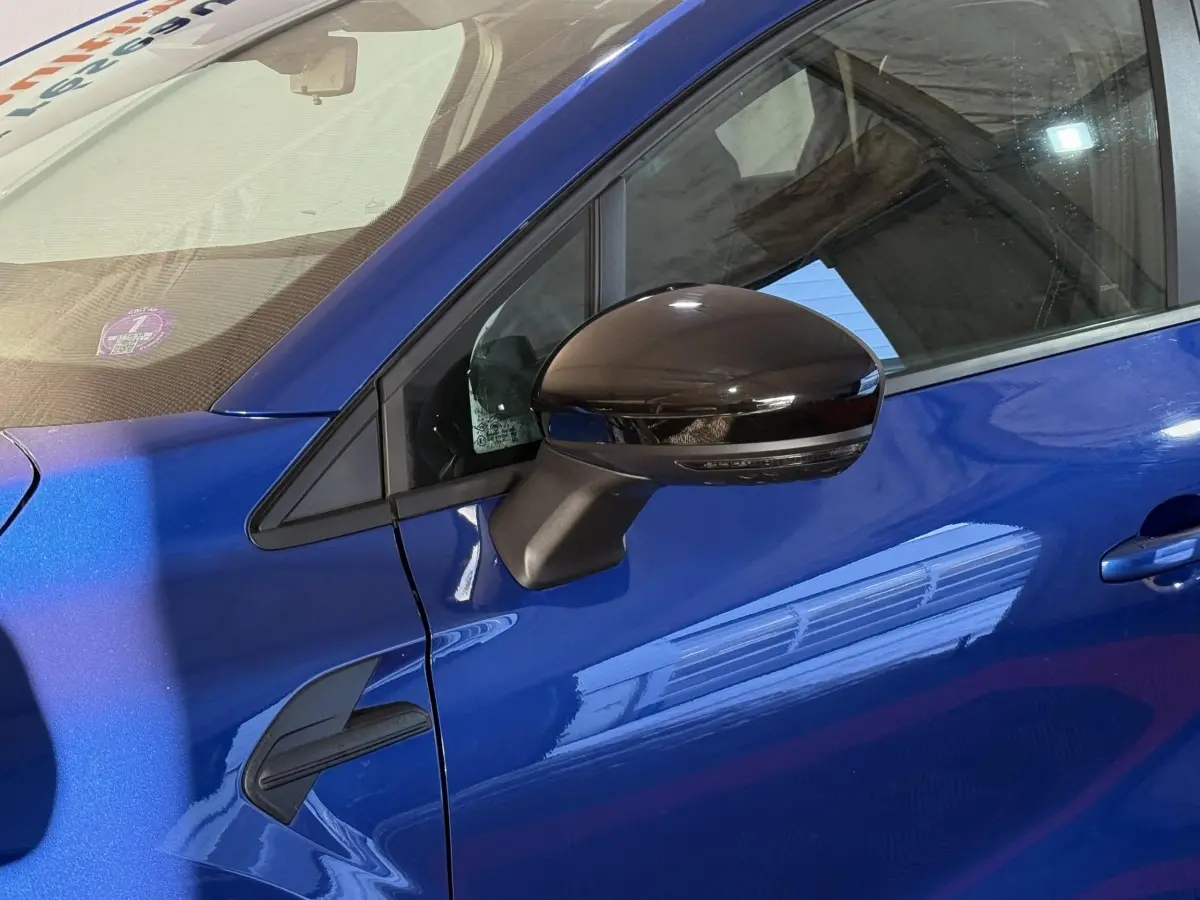 Détail du côté gauche d’un Renault Captur bleu 2024 avec rétroviseur noir brillant et poignée de porte visible.