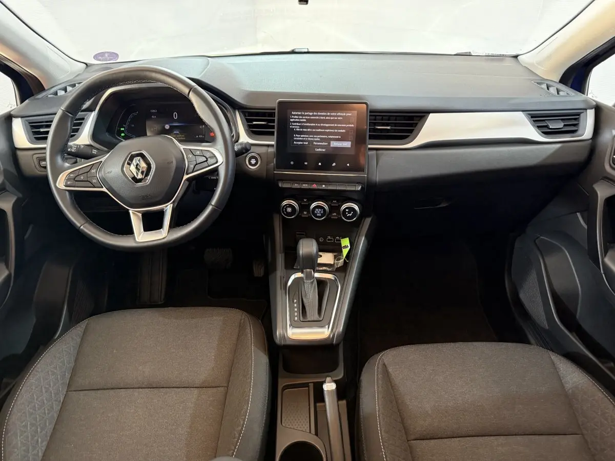 Vue intérieure avant du Renault Captur bleu 2024, volant multifonctions cuir synthétique et écran tactile central vertical.
