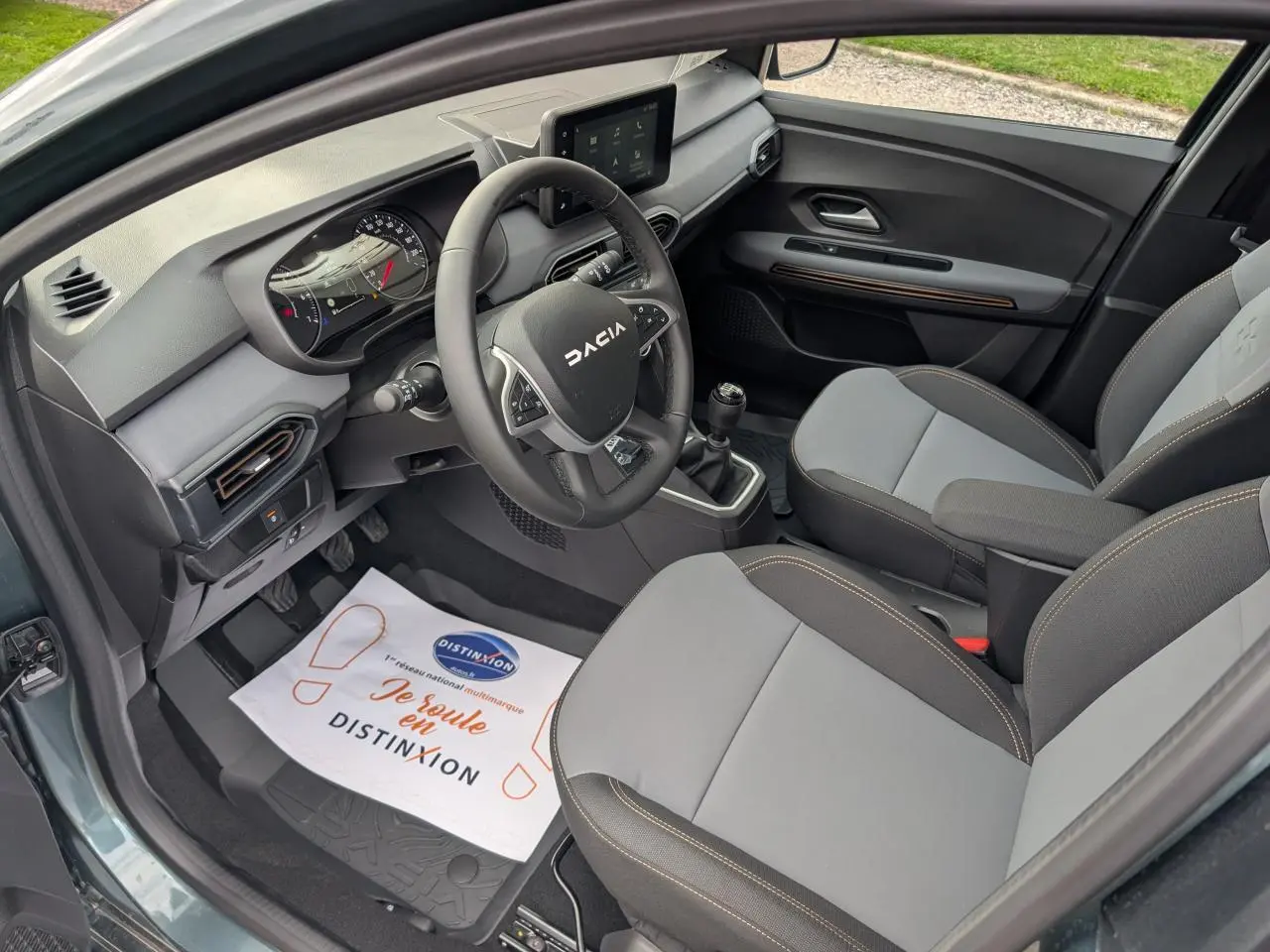 Vue intérieure côté conducteur du Dacia Jogger 2025 vert métallisé, avec volant, tableau de bord et sièges gris à surpiqûres brun cuivré.
