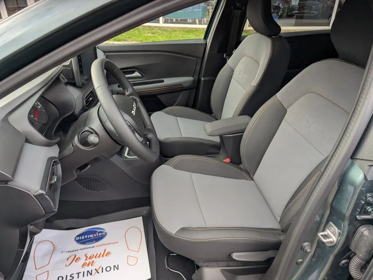 Vue intérieure côté conducteur du Dacia Jogger vert métallisé, montrant les sièges avant gris avec surpiqûres brun cuivré.