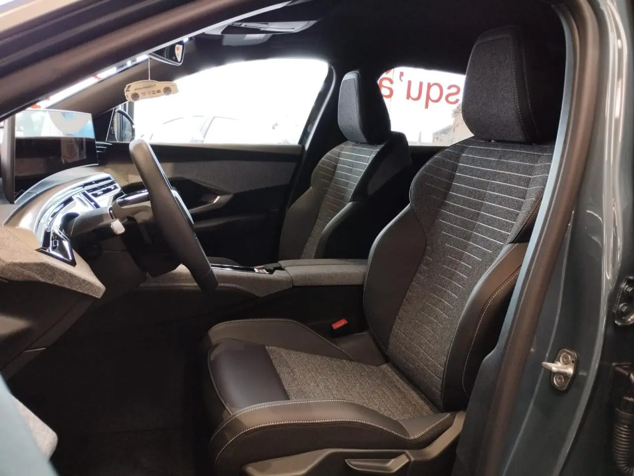 Vue intérieure côté gauche du Peugeot 3008 2025 avec sièges tissu gris et cuir noir, tableau de bord et écran incurvé flottant.