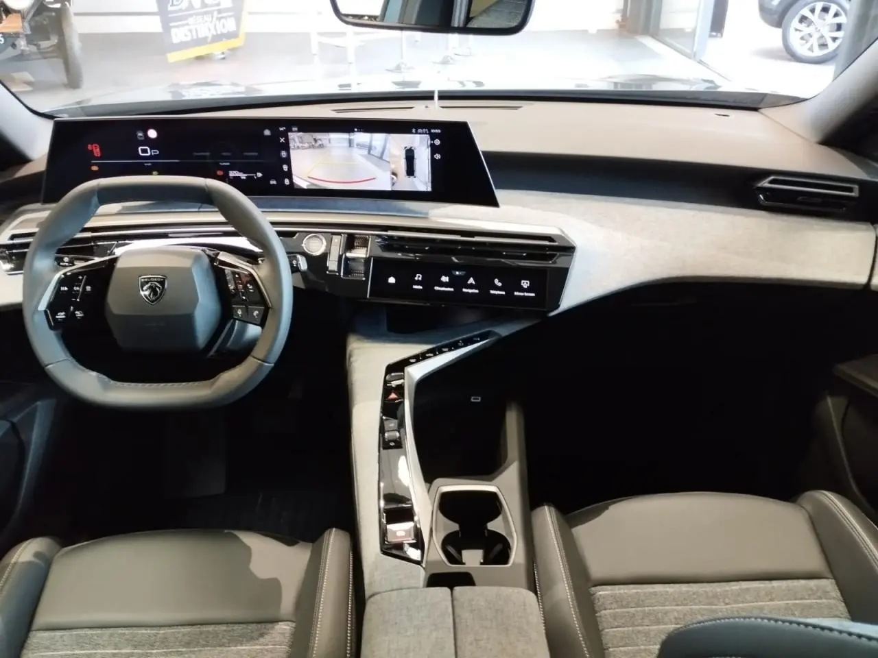 Vue intérieure avant du Peugeot 3008 2025 avec tableau de bord clair, écran incurvé flottant et volant compact noir.