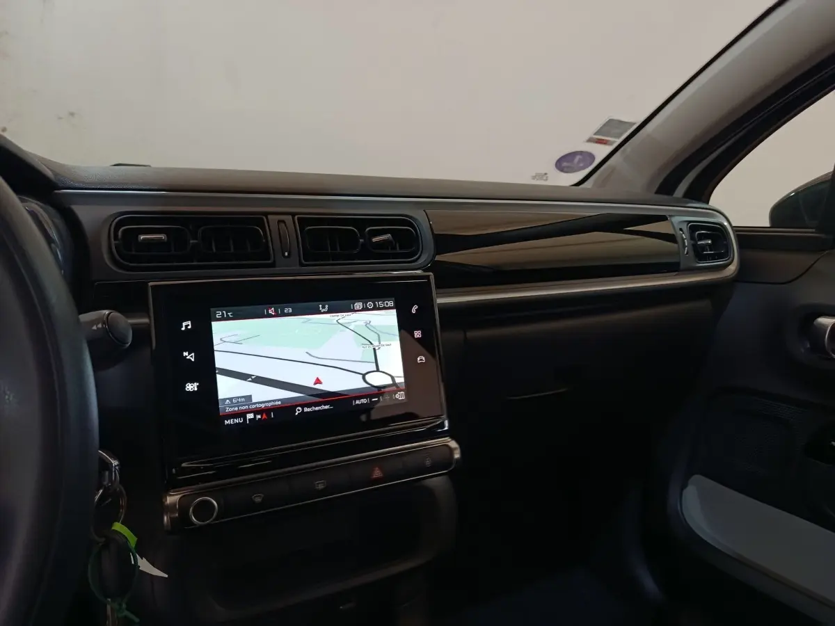 Vue intérieure côté passager du tableau de bord noir brillant avec écran tactile de navigation de la Citroën C3 blanche.