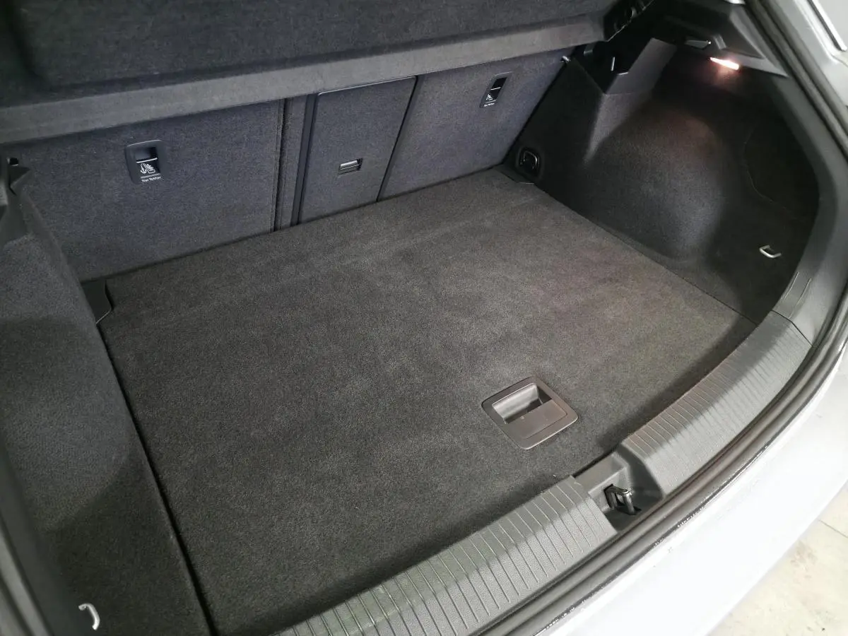 Coffre ouvert vu de l'arrière d'un Volkswagen T-Roc gris, montrant un espace de chargement propre et tapissé.