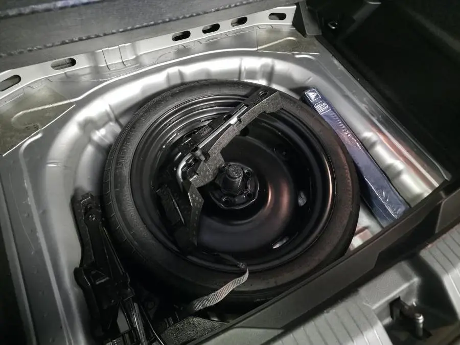 Vue rapprochée de la roue de secours noire et du cric dans le coffre du Volkswagen T-Roc gris 2022.