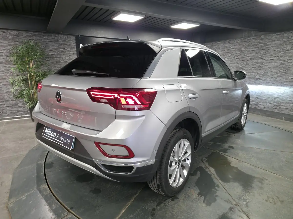 Volkswagen T-Roc gris métallisé vu en 3/4 arrière droit, avec feux arrière LED allumés et vitres surteintées.