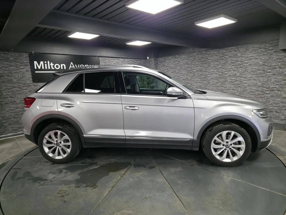 Vue latérale droite d'un Volkswagen T-Roc gris métallisé 2022, avec jantes alliage et barres de toit visibles.