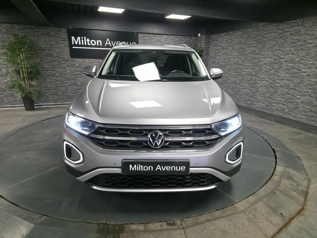 Vue avant d'un Volkswagen T-Roc gris métallisé avec feux LED allumés dans un showroom.