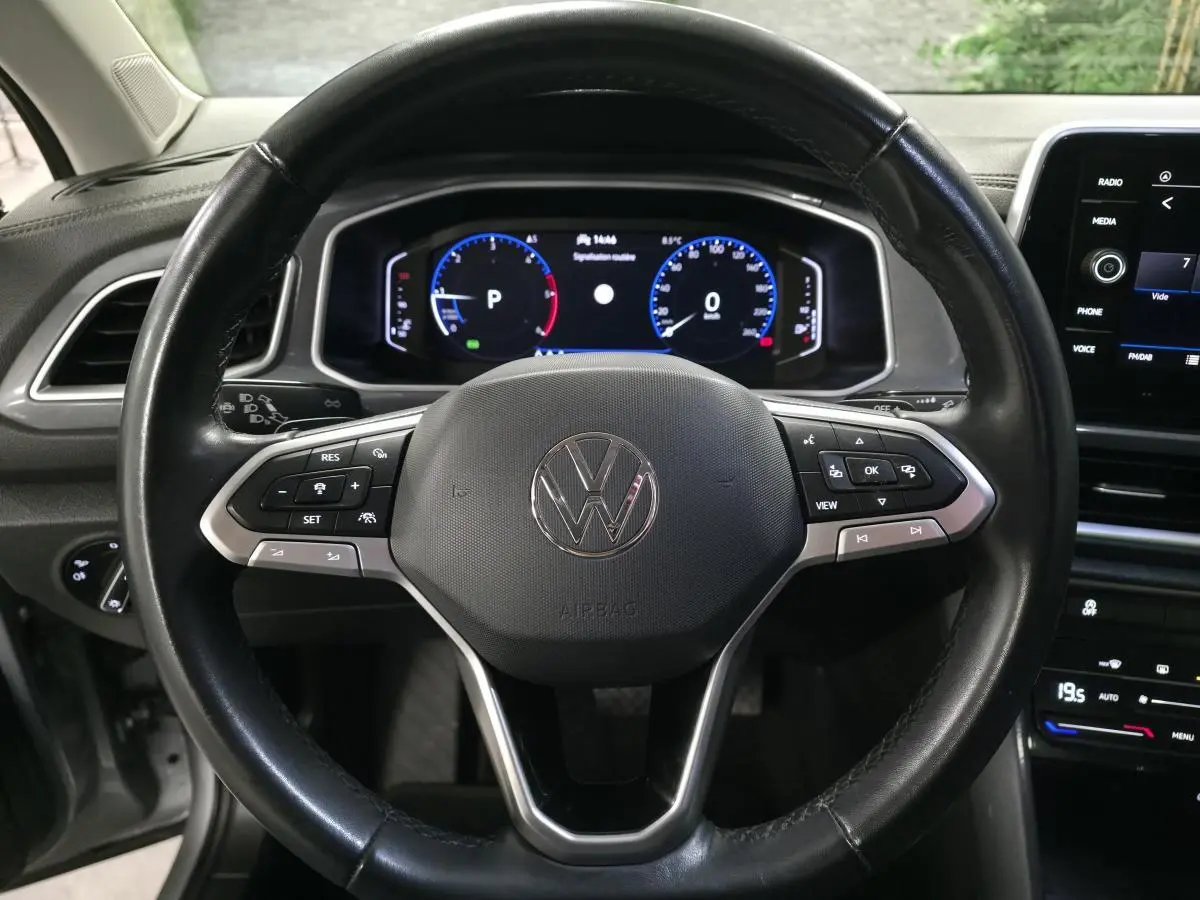 Vue rapprochée du volant en cuir noir avec commandes multifonctions d'un Volkswagen T-Roc 2022, tableau de bord digital visible.