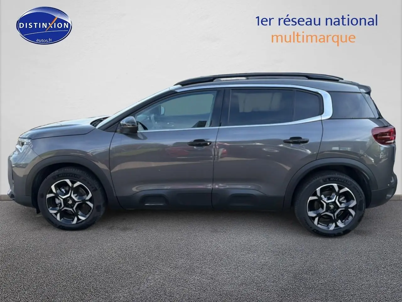 Vue latérale gauche d'un Citroën C5 Aircross gris platinium avec jantes alu et barres de toit noires.