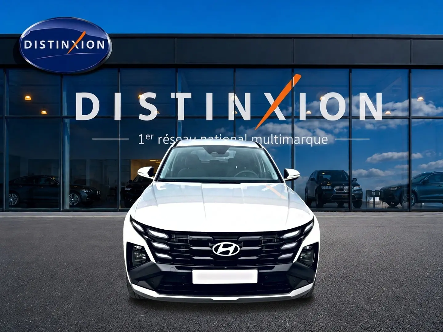 Vue avant d'un Hyundai Tucson blanc 2026 avec calandre noire distinctive, stationné devant une vitrine Distinxion.