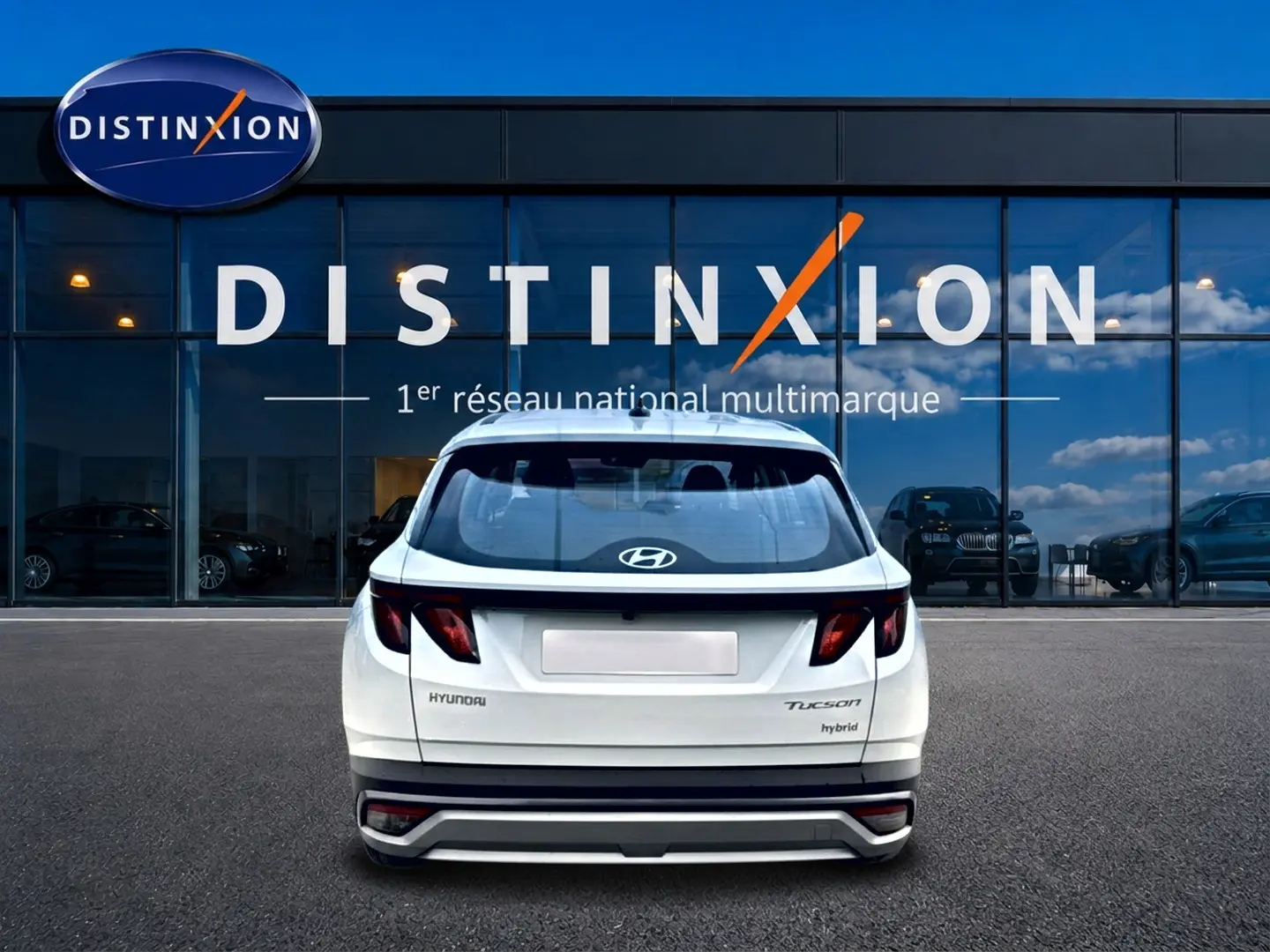 Vue arrière d'un Hyundai Tucson blanc hybride garé devant une vitrine avec logo Distinxion.