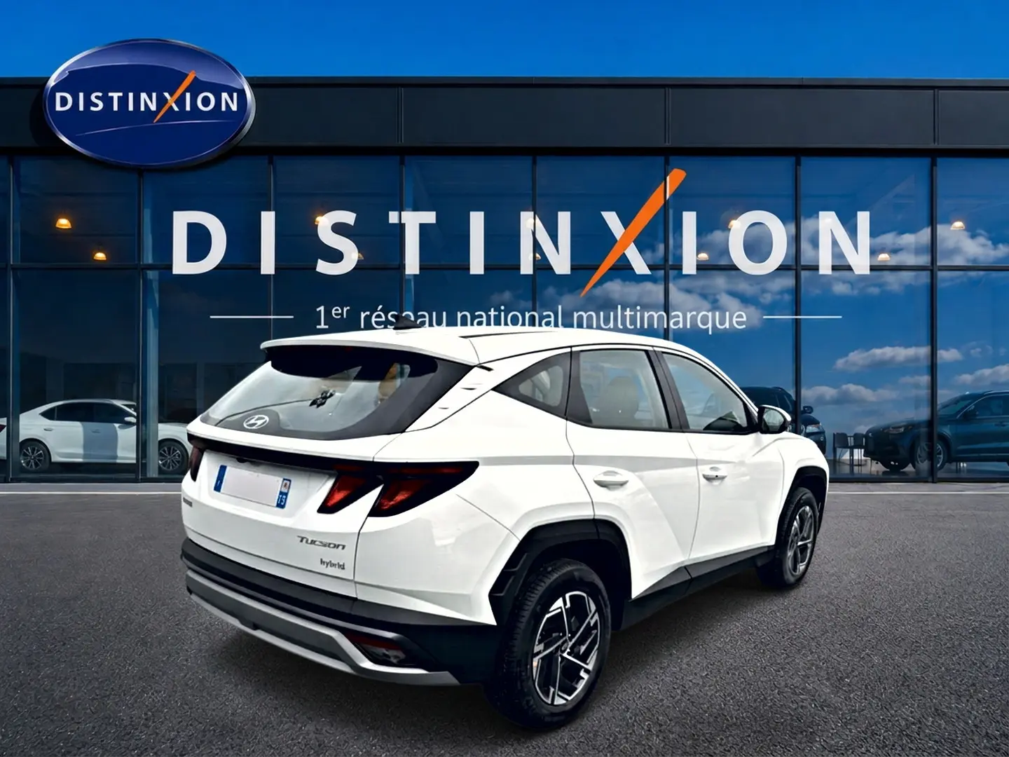 Vue 3/4 arrière droite d'un Hyundai Tucson blanc hybride 2026 avec jantes alliage 17 pouces devant une vitrine Distinxion.