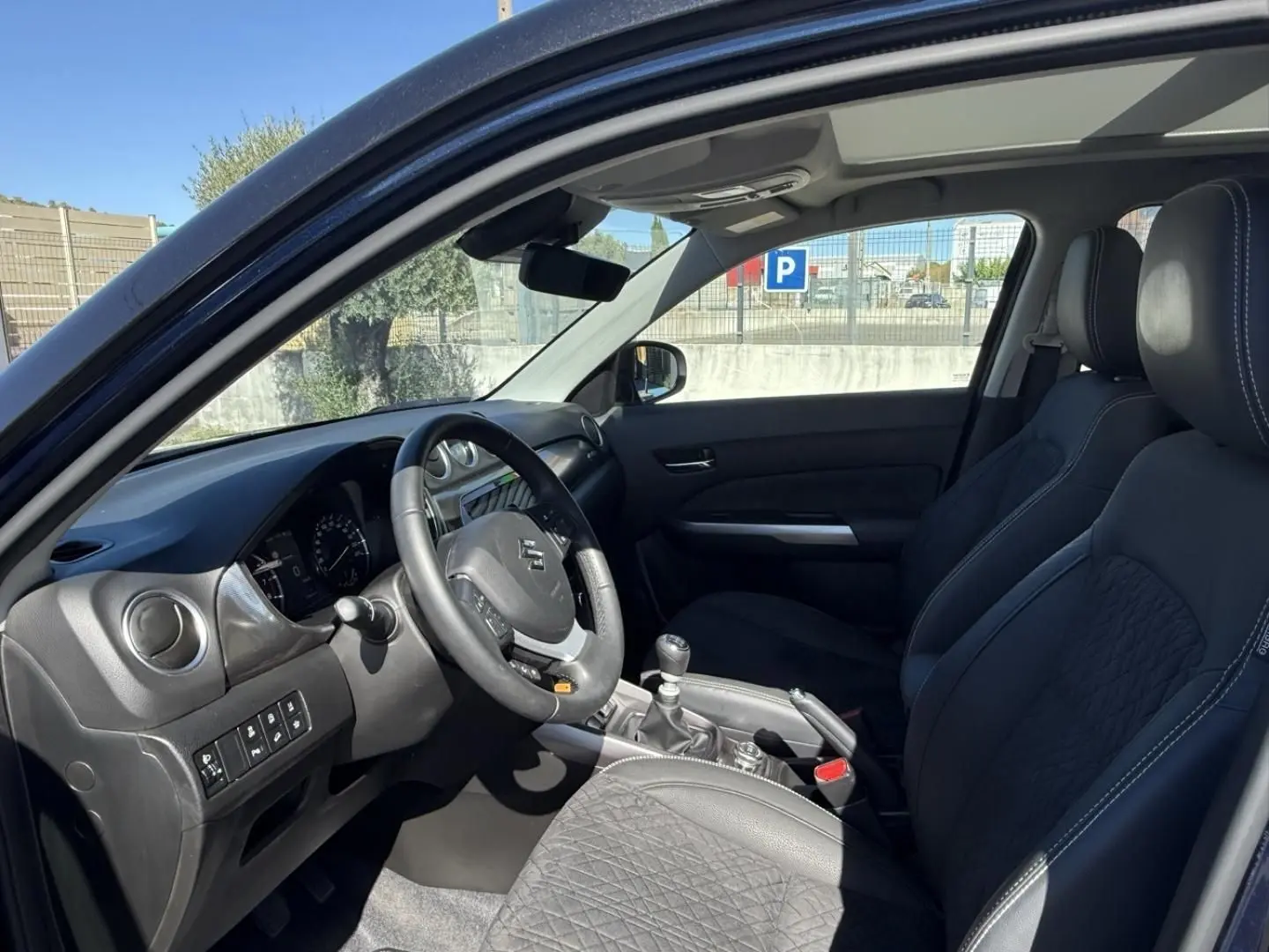 Vue intérieure côté conducteur du Suzuki Vitara 2025 bleu foncé, montrant le volant, la boîte manuelle et les sièges noirs.