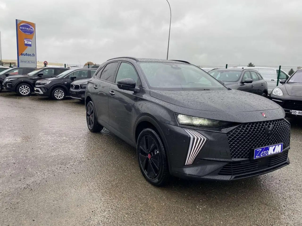 DS7 Crossback gris foncé en 3/4 avant droit sous la pluie, avec calandre large et feux LED distinctifs allumés.