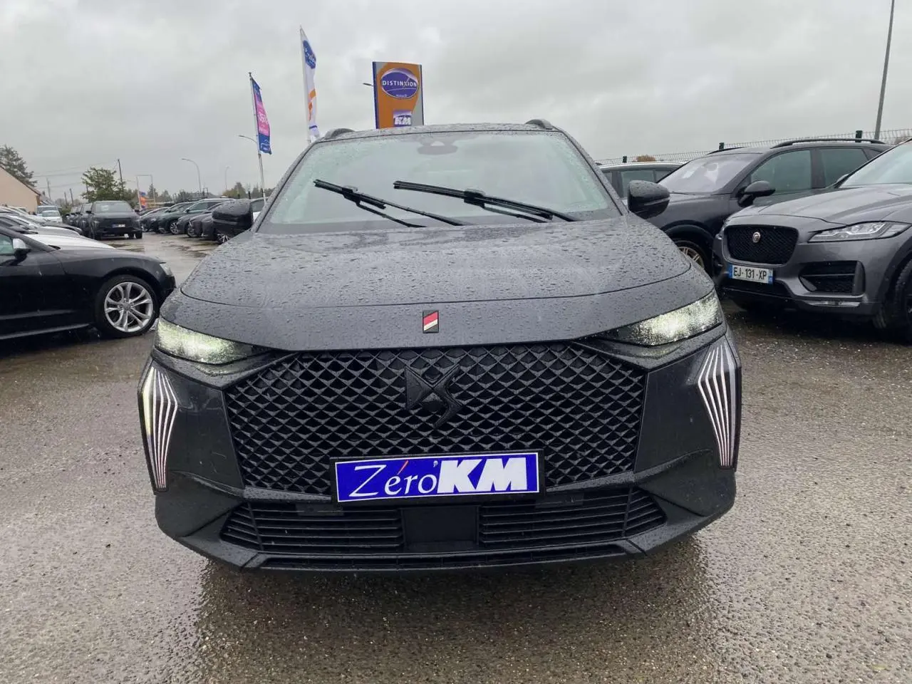 Vue avant d'un DS7 Crossback gris foncé 2024 avec calandre noire et feux LED verticaux allumés sous la pluie.