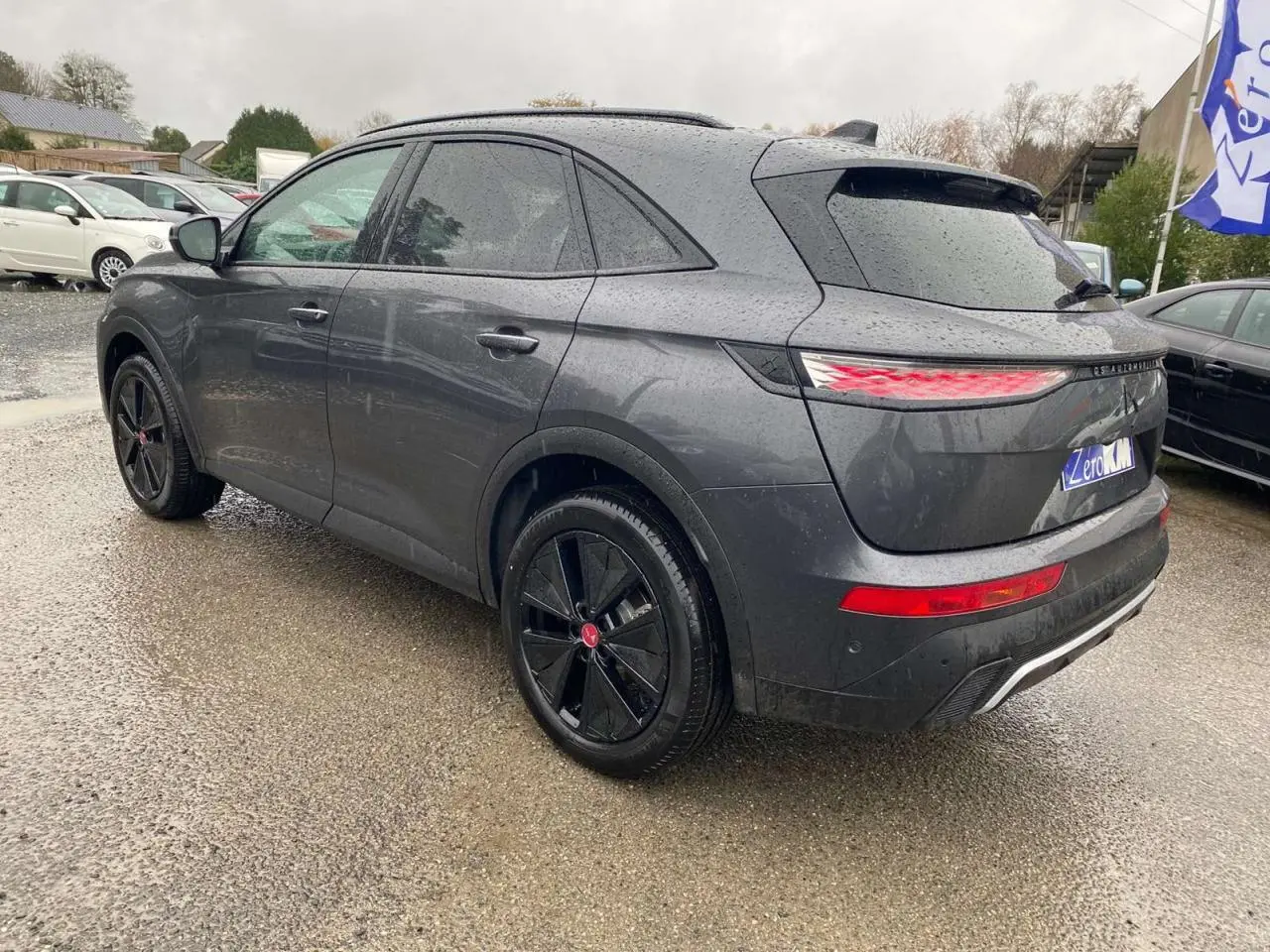 Vue 3/4 arrière droite d’un DS7 Crossback gris foncé 2024 avec jantes noires et feux arrière LED allumés.