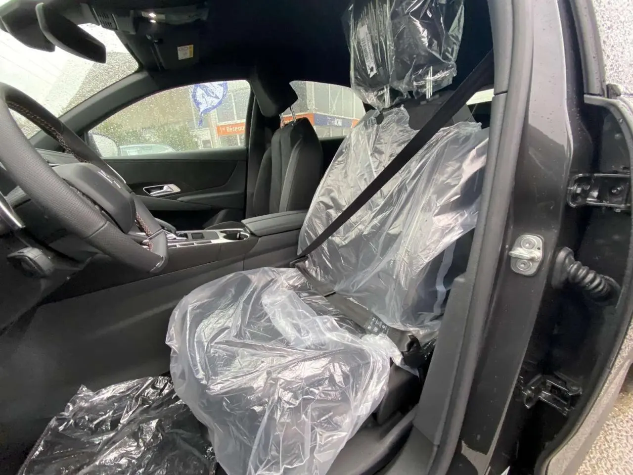 Vue intérieure côté conducteur du DS7 Crossback gris foncé 2024, siège avant protégé par une housse plastique.