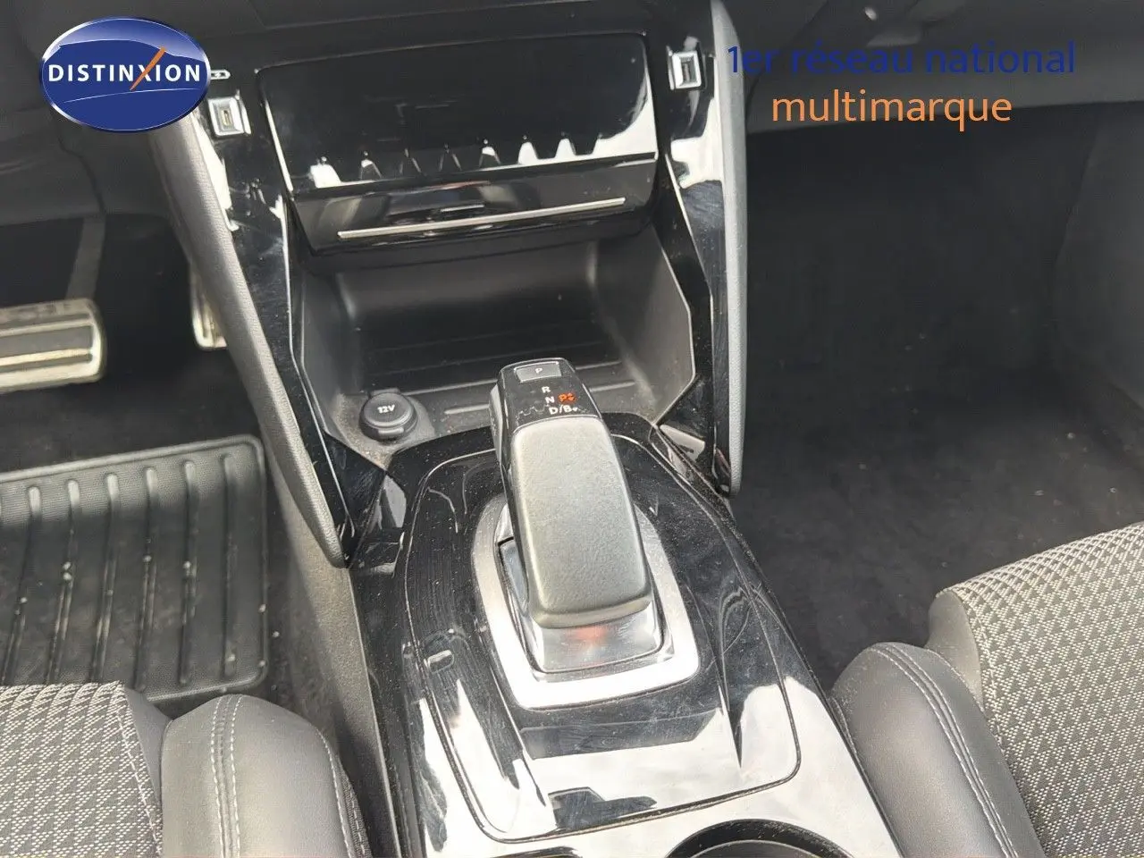 Le levier de vitesses automatique noir brillant au centre de la console d'une Peugeot 208 électrique, vue intérieure rapprochée.