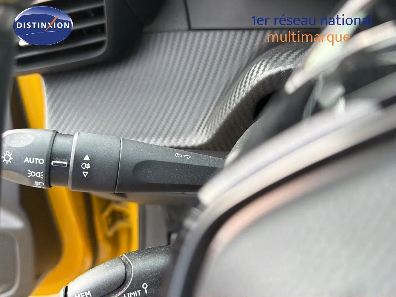 Gros plan sur la commande des feux et clignotants côté gauche du volant d'une Peugeot 208 électrique jaune Faro métal avec toit noir.