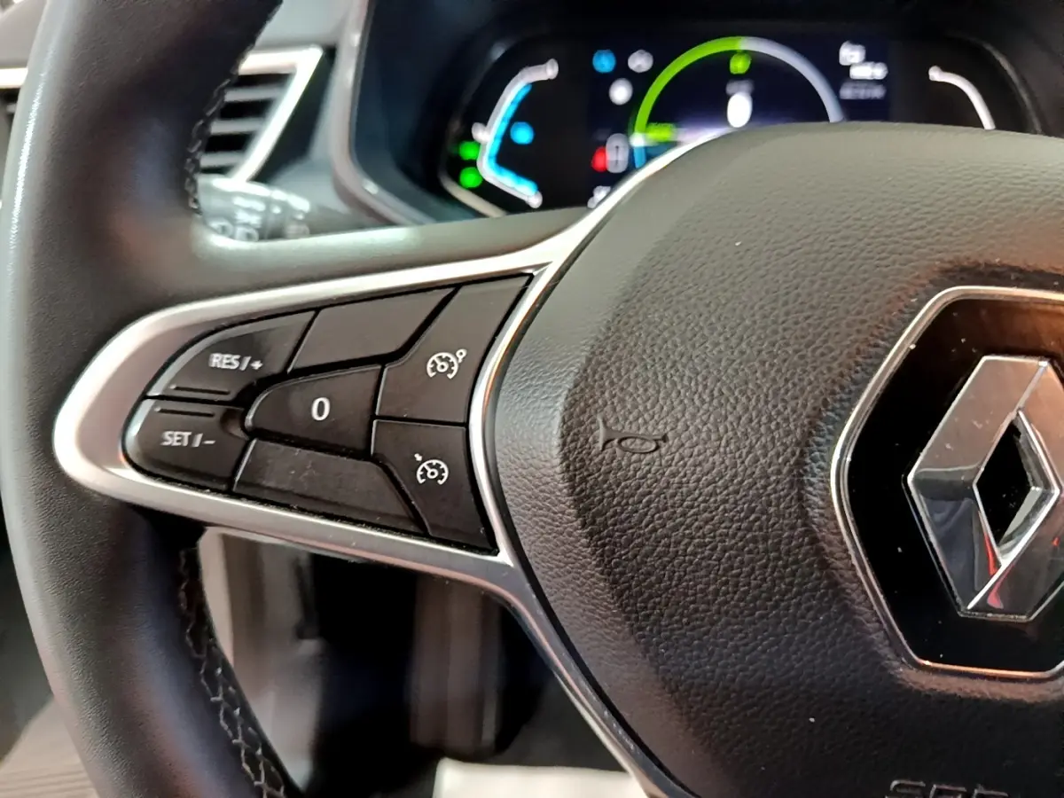 Gros plan sur le volant cuir synthétique de la Renault Clio Business E-TECH 140, avec commandes de régulateur de vitesse visibles.