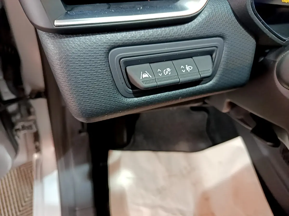 Gros plan sur les commandes d'assistance à la conduite sous le tableau de bord côté gauche de la Renault Clio Business E-TECH 140 gris foncé.