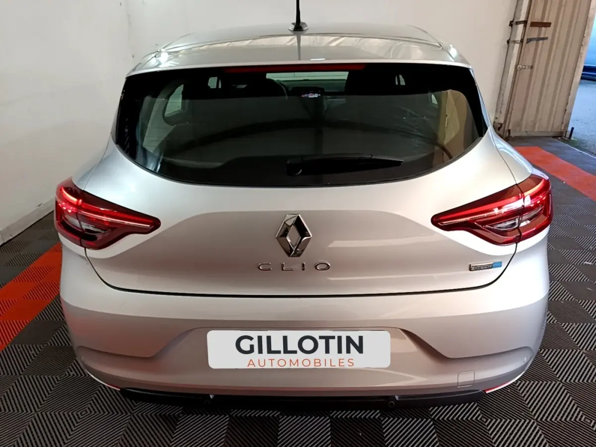 Vue arrière d'une Renault Clio gris clair avec feux LED allumés, dans un garage au sol carrelé noir et orange.