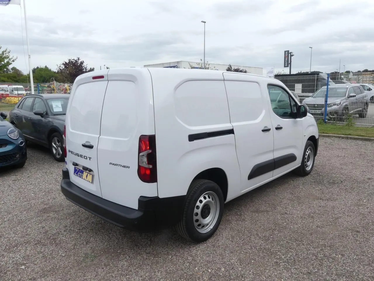 Peugeot Partner blanc vue 3/4 arrière droit, porte latérale coulissante et jantes tôles grises visibles.