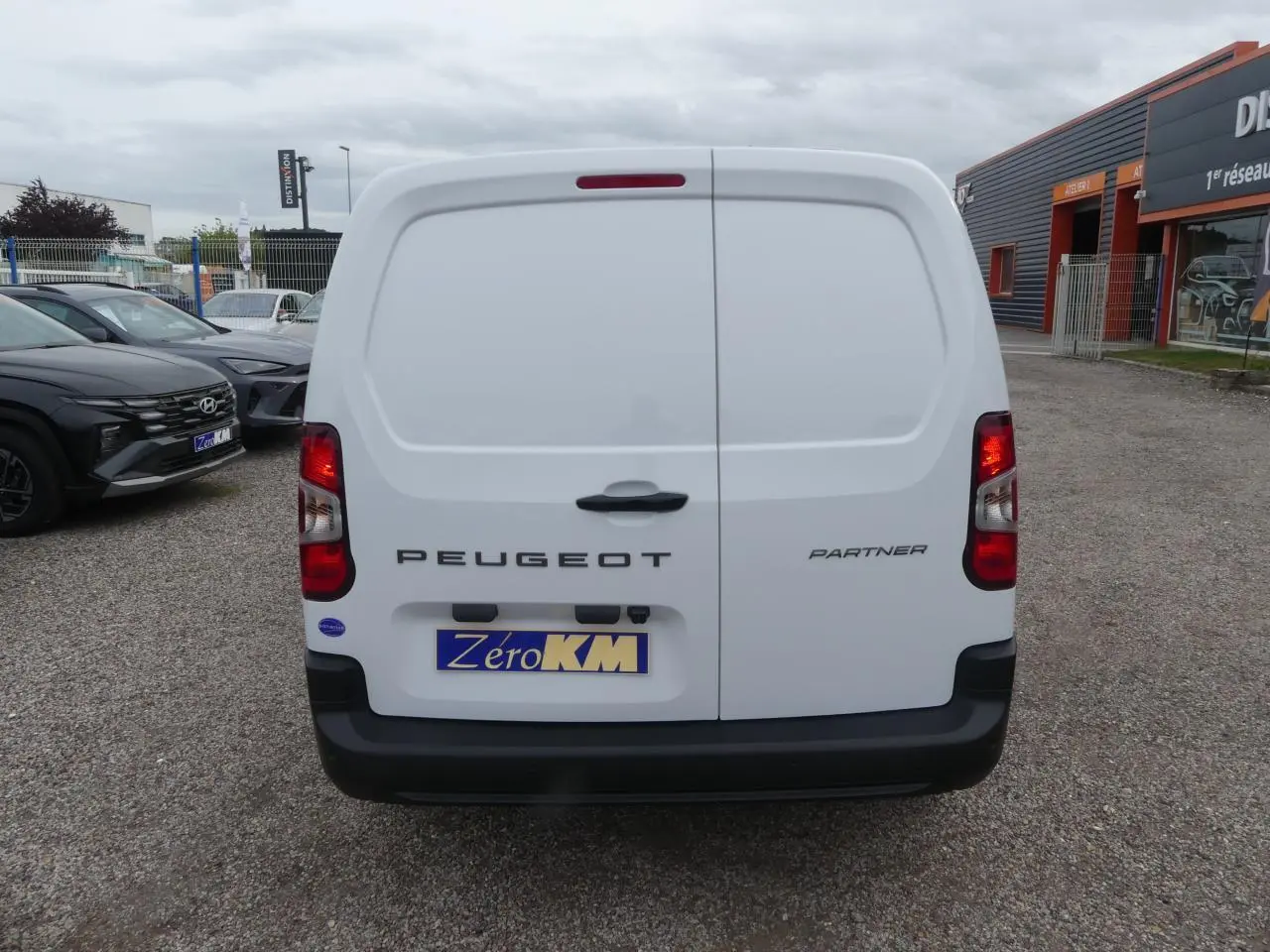 Vue arrière d'un Peugeot Partner blanc 2025 avec portes battantes et logo visible sur un parking extérieur.