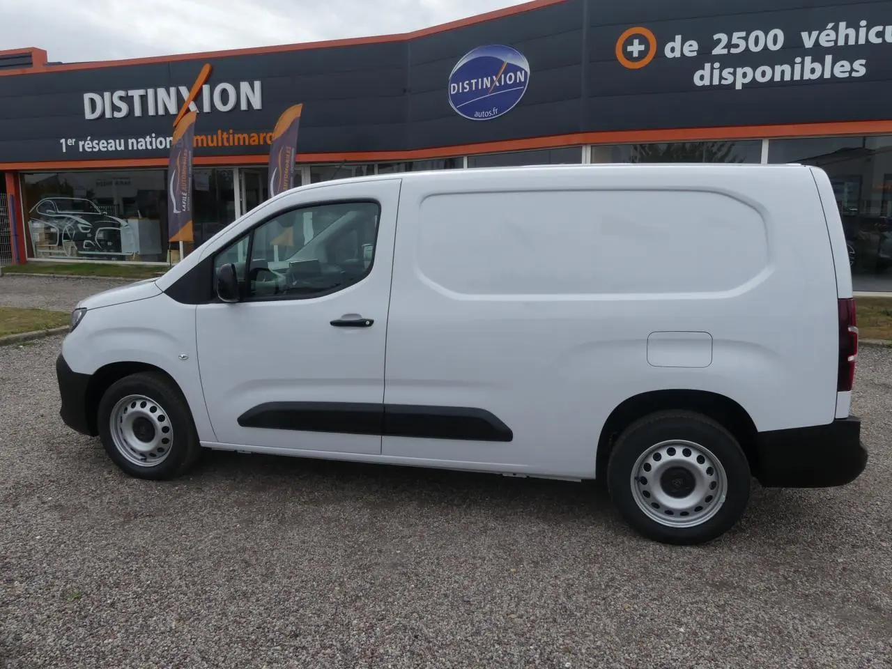 Vue de profil côté gauche d’un utilitaire Peugeot Partner blanc avec jantes tôles et protections noires sur porte latérale coulissante.