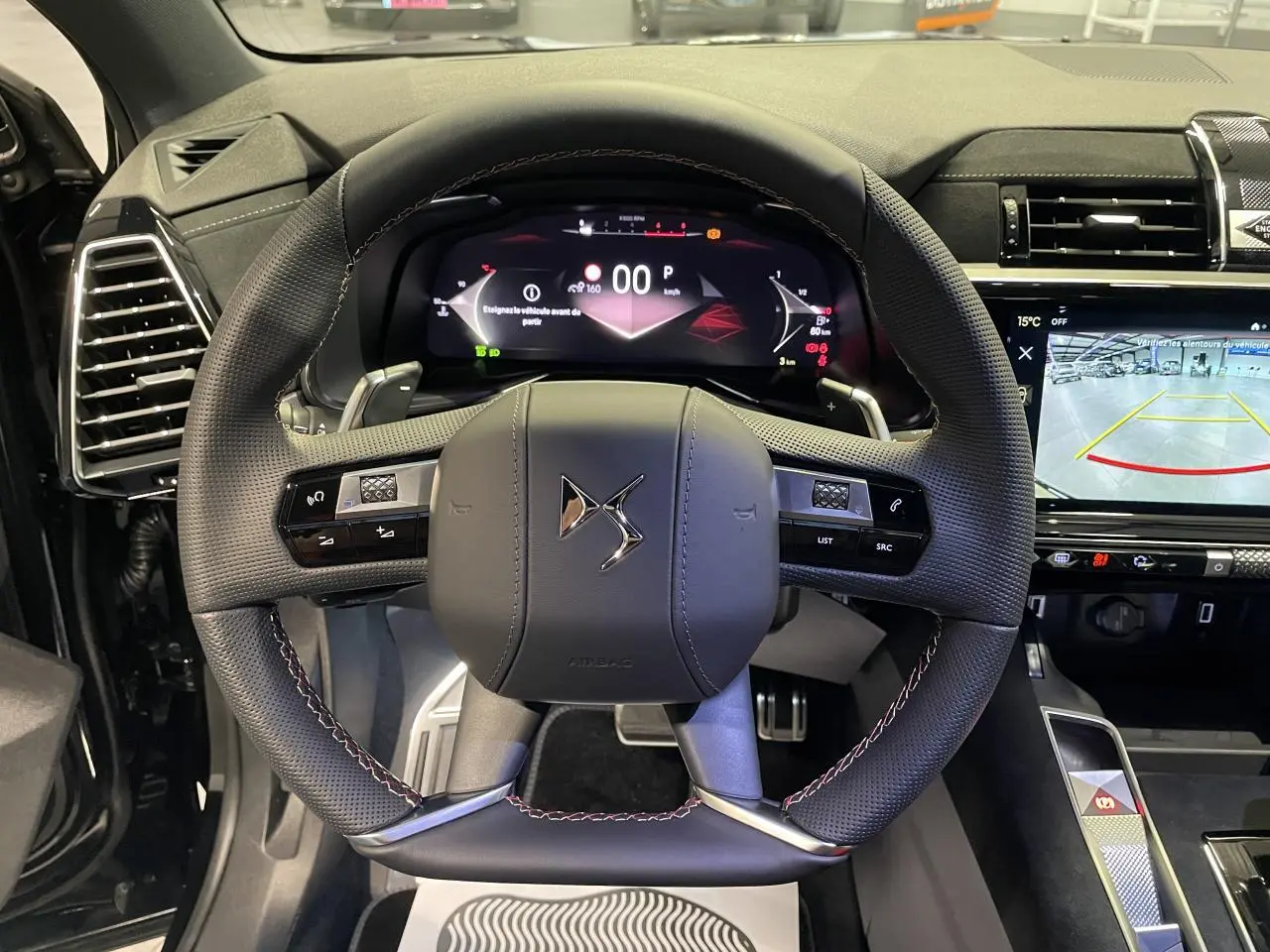 Vue intérieure centrée sur le volant DS en cuir perforé avec coutures rouges et tableau de bord numérique du DS7 Crossback noir.