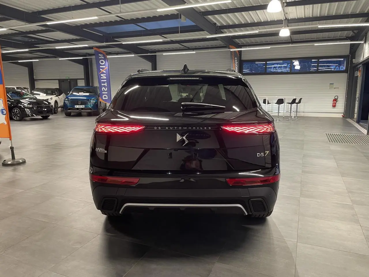 Vue arrière d'un DS7 Crossback noir métallisé avec feux arrière LED allumés dans un showroom.