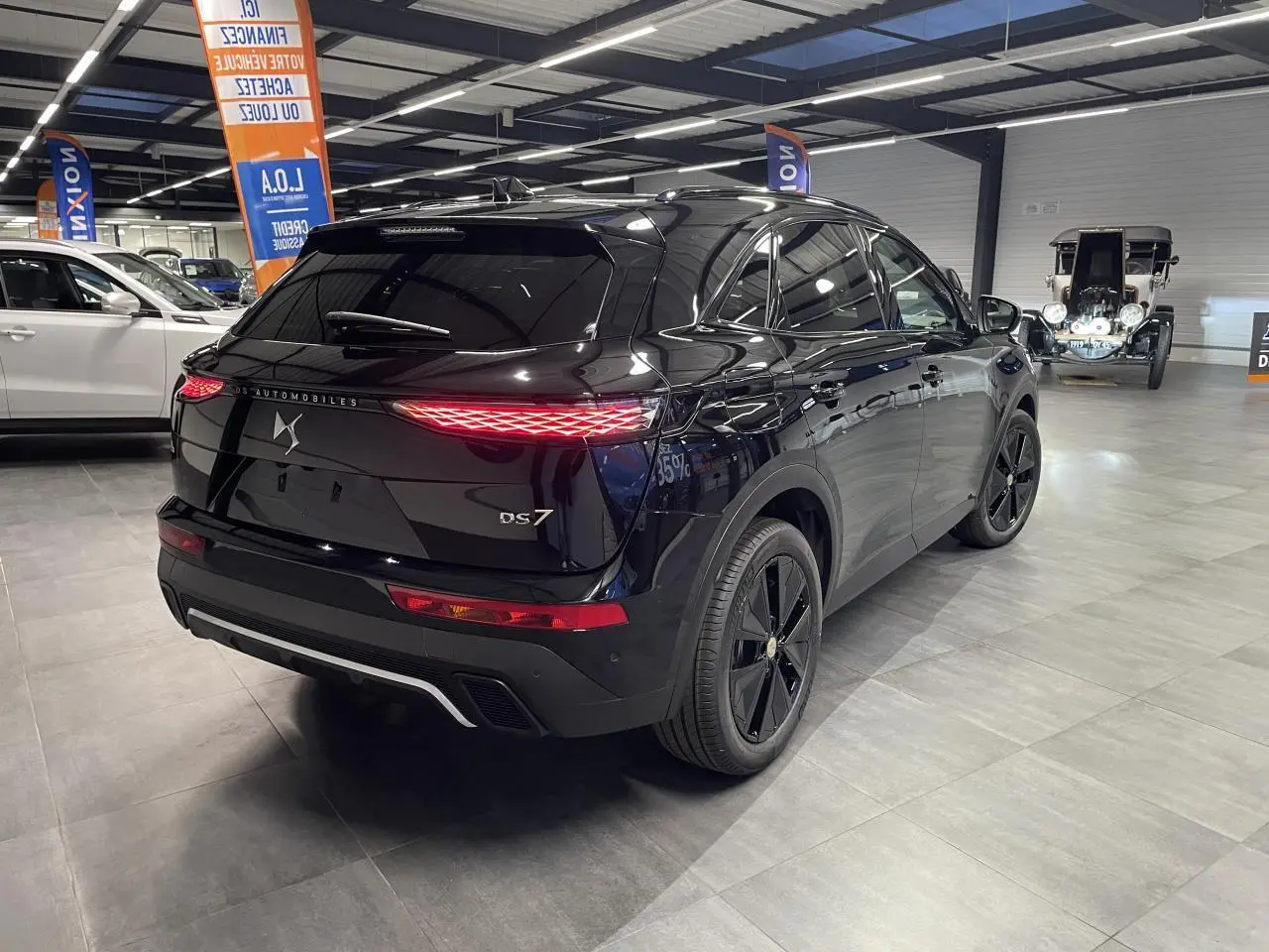 Vue 3/4 arrière droite d'un DS7 Crossback noir métallisé avec feux arrière LED et jantes noires en showroom.