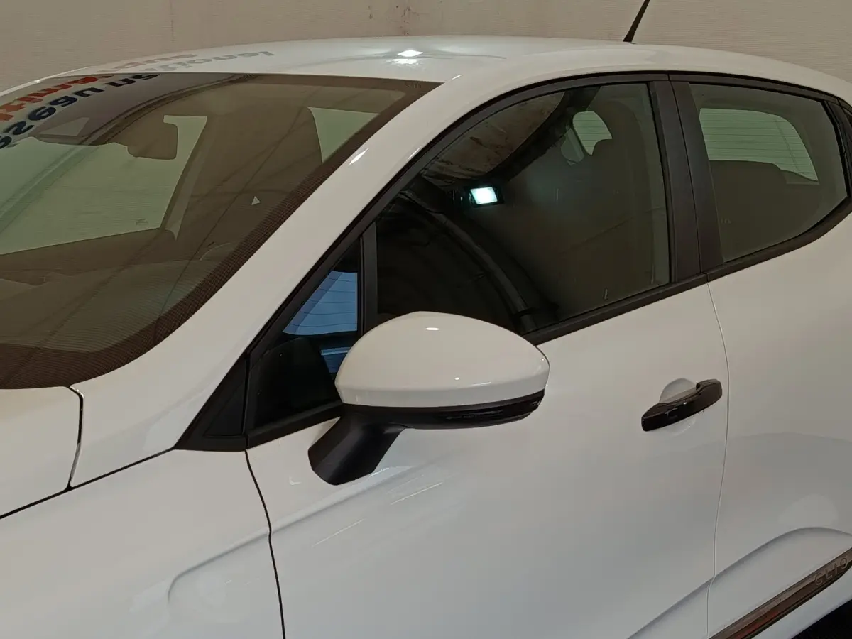 Vue latérale côté gauche d'une Renault Clio Business blanche 2021, mettant en valeur la poignée de porte et le rétroviseur extérieur.