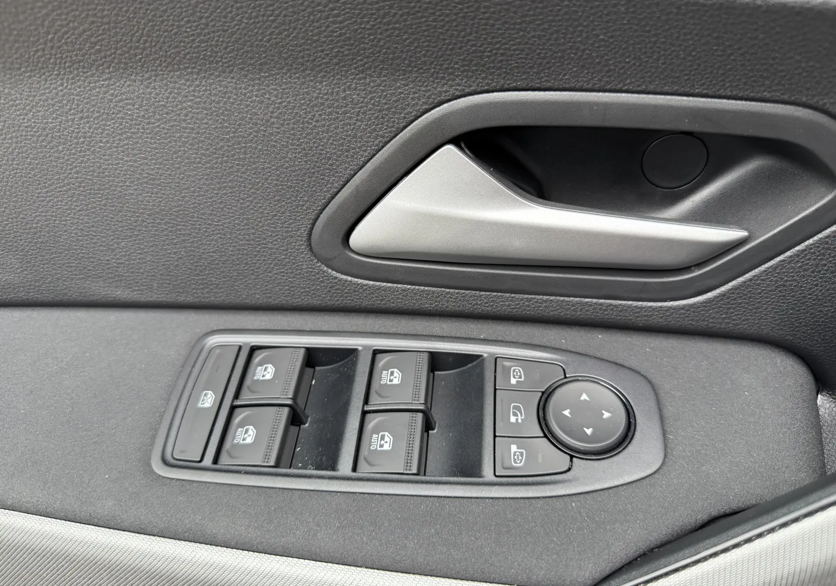 Gros plan sur la commande des vitres et le bouton de réglage des rétroviseurs côté conducteur d’un Dacia Bigster gris schiste.