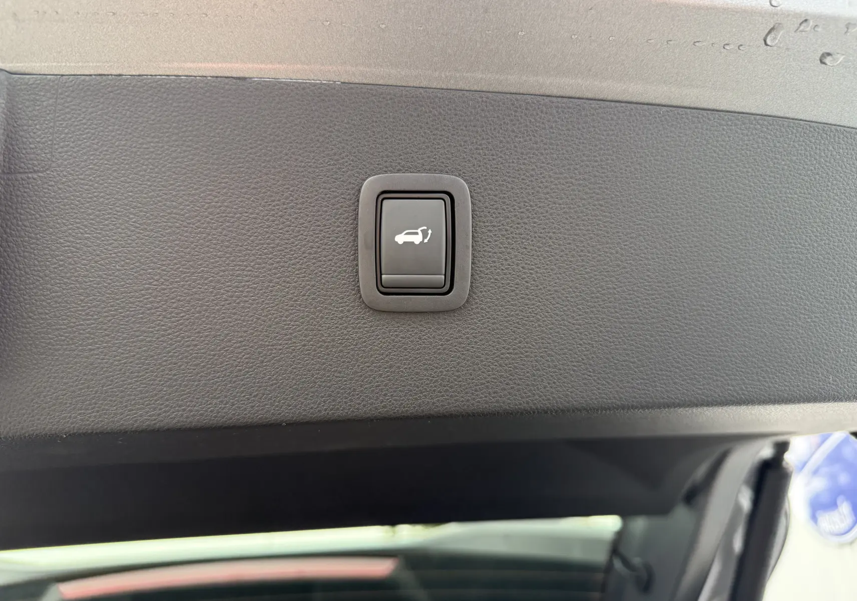 Bouton de fermeture électrique du coffre sur la garniture intérieure du hayon du Dacia Bigster gris schiste.