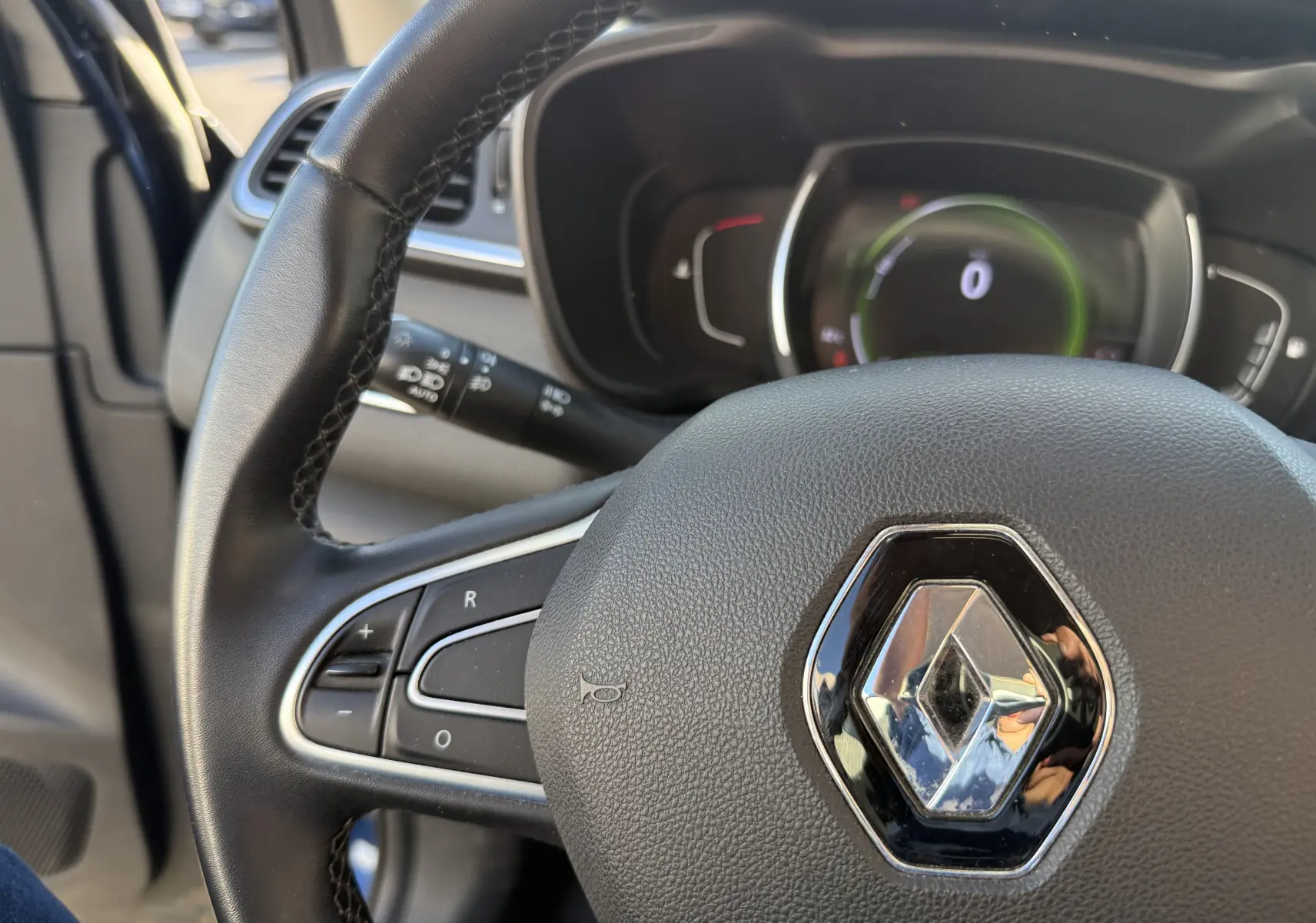 Vue rapprochée du volant noir avec logo Renault du Renault Kadjar bleu, tableau de bord numérique en arrière-plan.
