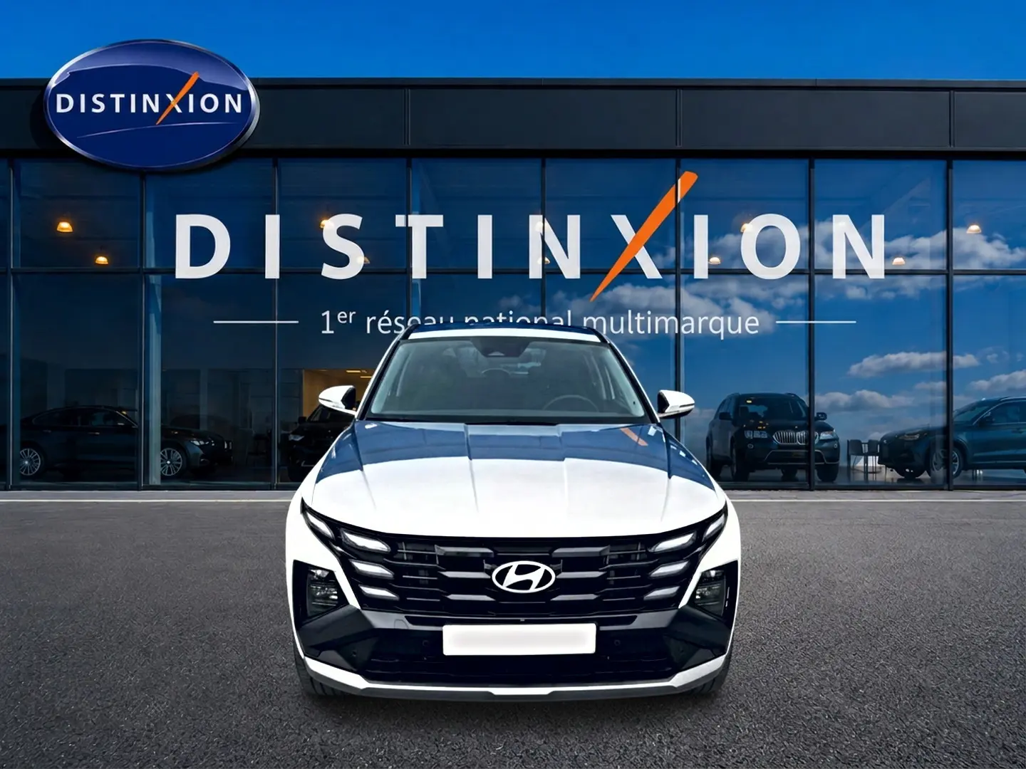 Vue frontale d'un Hyundai Tucson blanc 2026 avec calandre noire et logo Hyundai bien visible, devant une vitrine Distinxion.