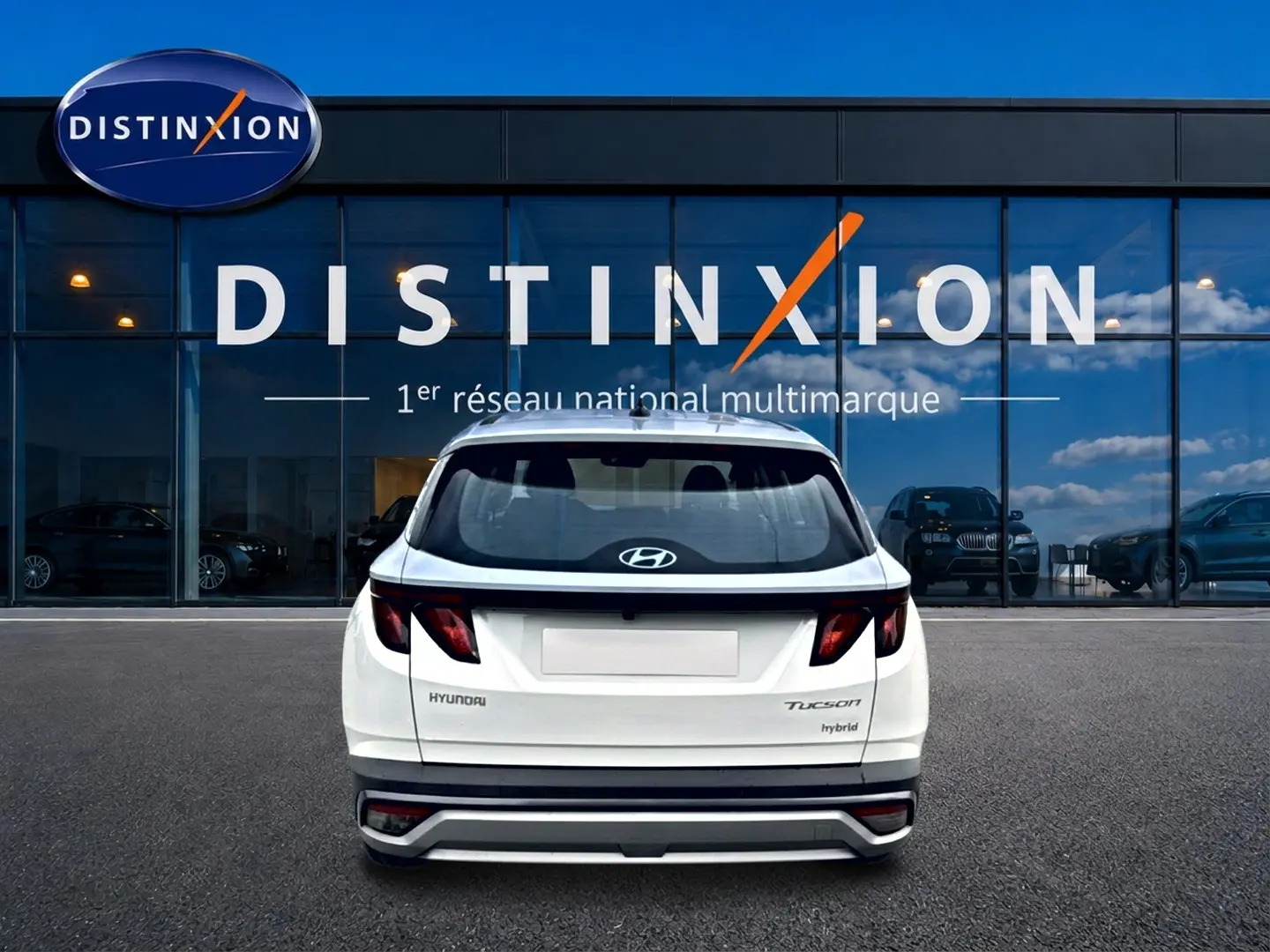 Vue arrière d'un Hyundai Tucson hybride blanc 2026 garé devant une vitrine avec logo Distinxion.
