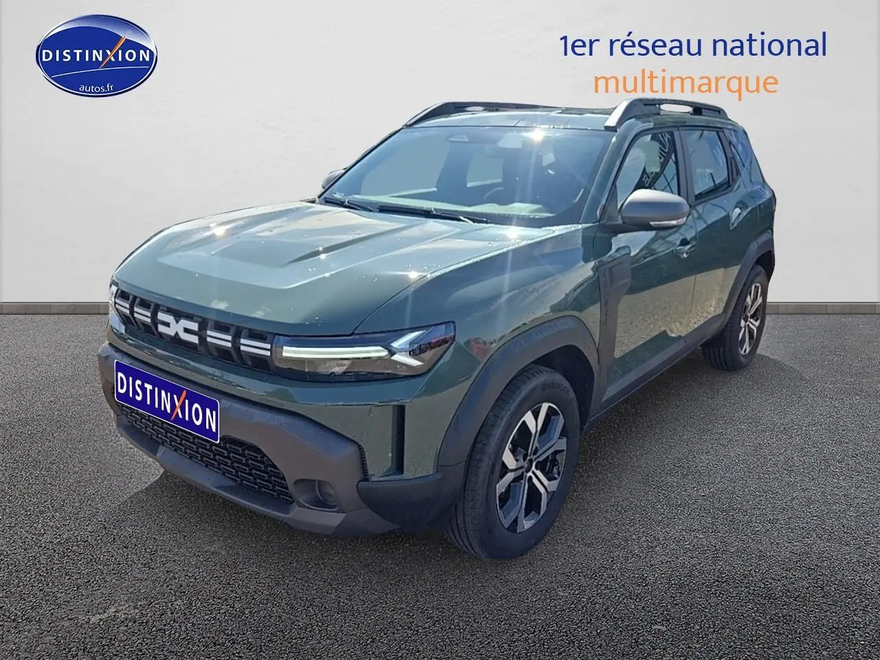 Dacia Duster vert kaki en 3/4 avant droit avec barres de toit et jantes alu visibles sur fond neutre.