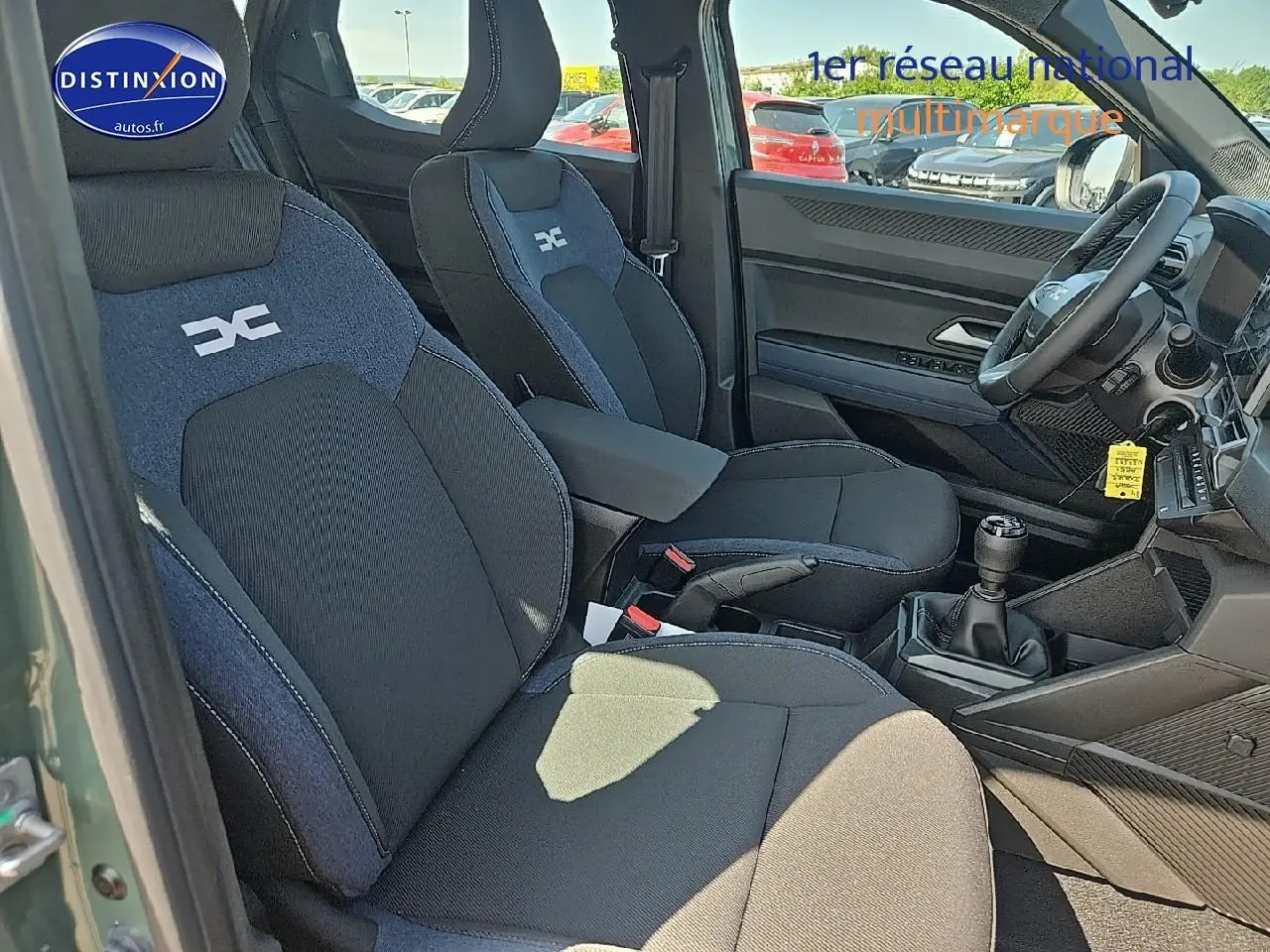 Intérieur avant droit du Dacia Duster 2025 vert kaki, sièges tissu noir et bleu avec accoudoir central et boîte manuelle.