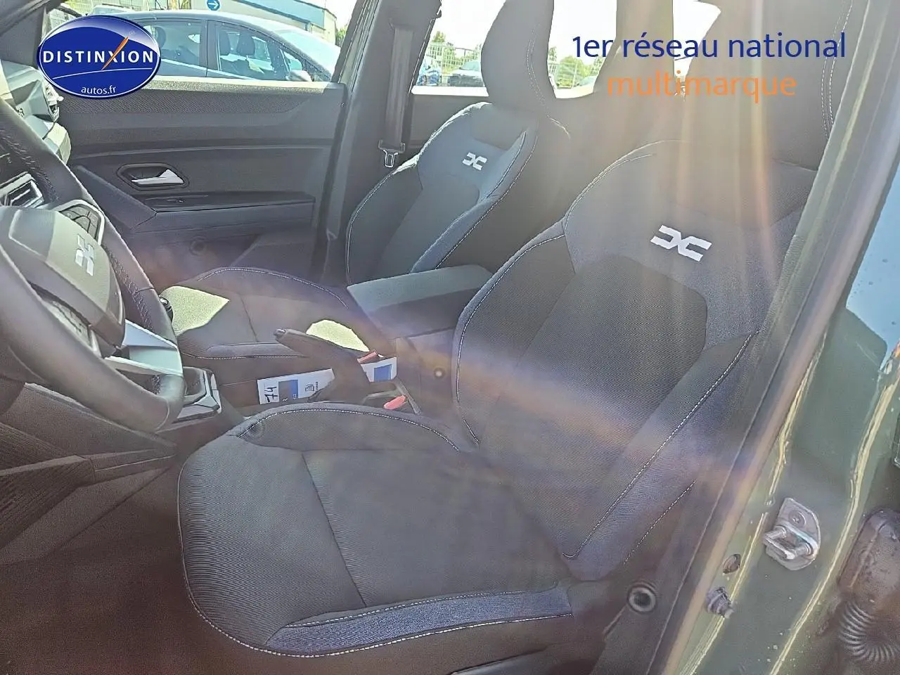 Vue intérieure côté conducteur du Dacia Duster 2025 vert kaki, sièges noirs avec logo DC brodé et accoudoir central.