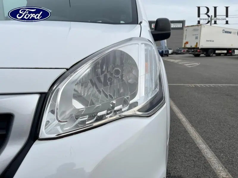 Gros plan sur le phare avant droit blanc banquise d'un Peugeot Partner Tepee 2016, vue en extérieur sur parking.