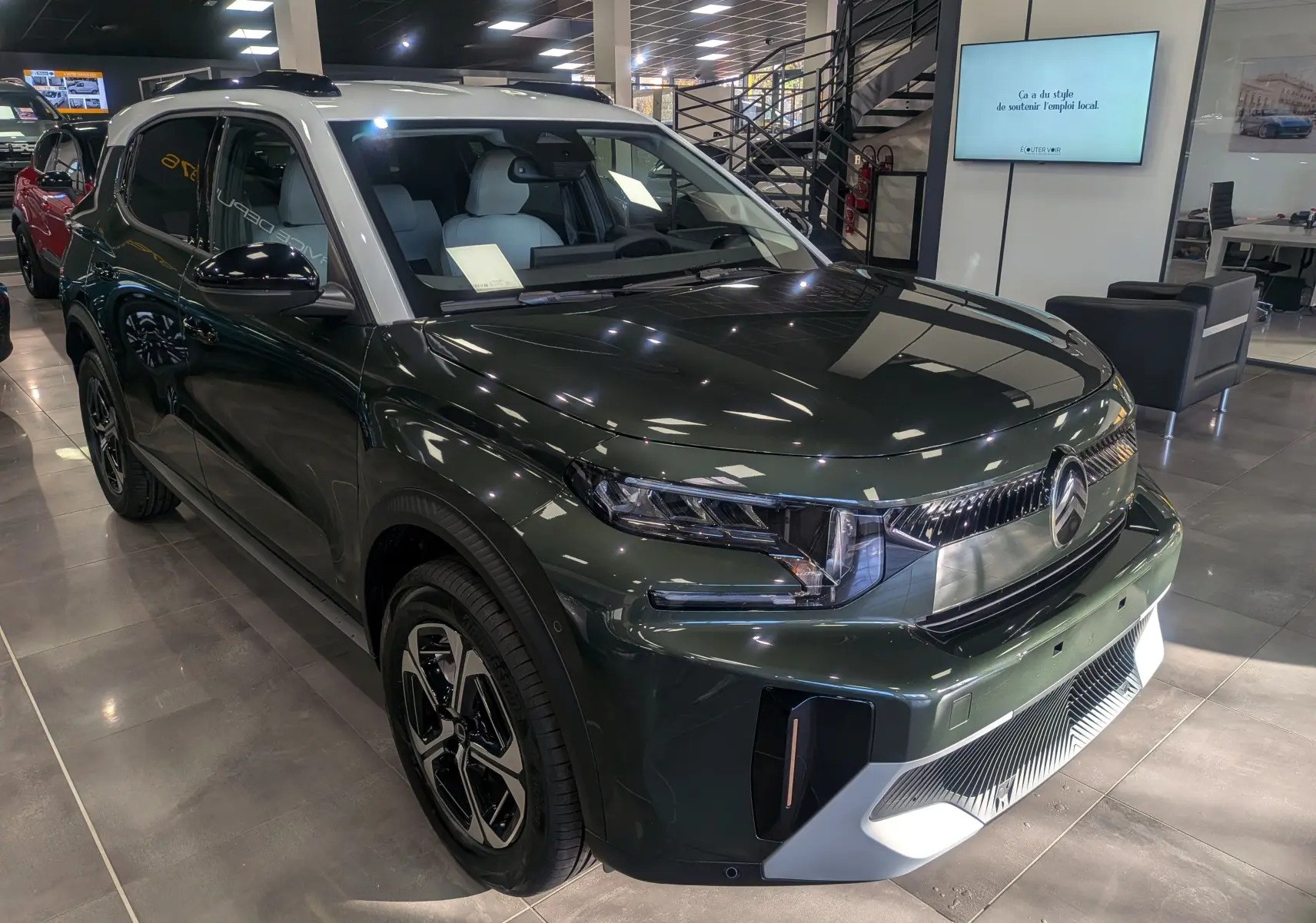 Vue 3/4 avant gauche d'un Citroën C3 Aircross 2025 vert Montana avec toit blanc en showroom lumineux.