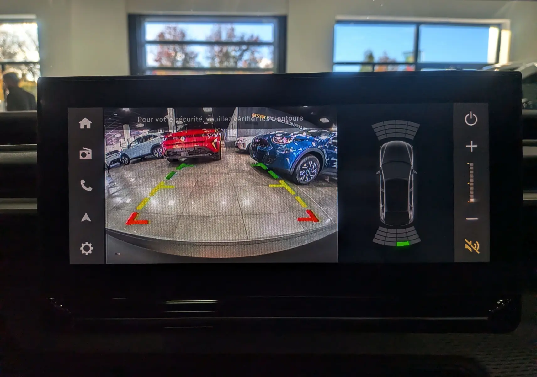 Écran de caméra de recul montrant un intérieur de garage avec plusieurs véhicules dont un Citroën C3 Aircross vert Montana à toit blanc.