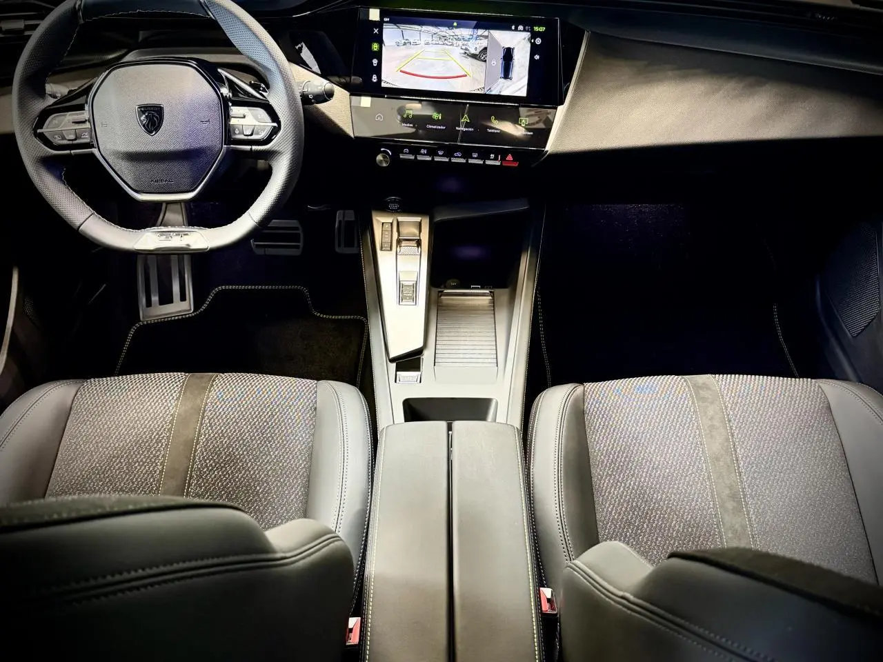 Vue intérieure avant de la Peugeot 308 GT 2025, montrant le volant cuir, la console centrale et les sièges tissu/TEP gris.